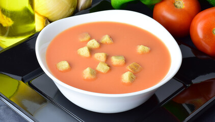 Close up. Andalusian homemade gazpacho, from Spain, served on a white plate with breads and exposed with its ingredients, the fundamental base of tomato. Healthy and beneficial.	