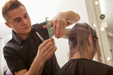 Obraz na płótnie Canvas Handsome hairdresser cutting woman hair with professional scissors