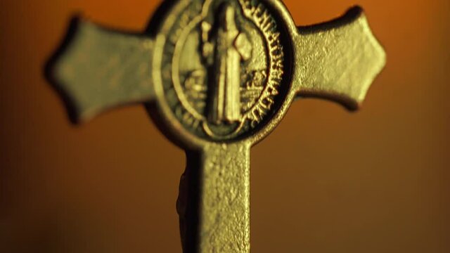 Tilt soft-focus shot of a Saint Benedict rosary with the candle burning in the background