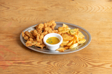 Tray of chicken fingers in batter with egg and breadcrumbs, parsley, sweet curry sauce and homemade chips on a metal tray