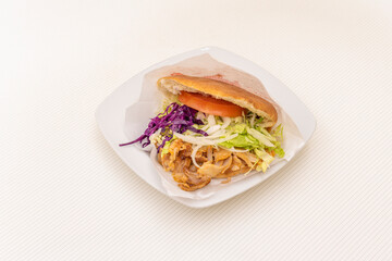 Grilled chicken doner kebab sandwich with onion, purple cabbage, lettuce and tomato with yogurt and tomato sauce on white table