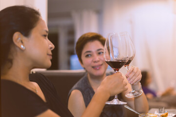 Friend toasting with glasses of red wine at dinner party.