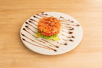 Norwegian salmon tartare, layer of tomato cubes and lettuce cpa with soy sauce on white plate