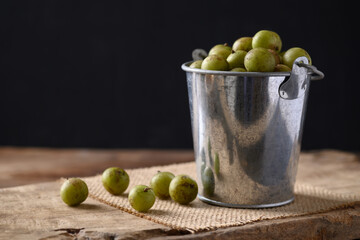Wild Indian gooseberry or amla in a silver bucket on wooden with black background, Fruit tree in Asia use in various cuisine, herbal medicine and rich vitamin C
