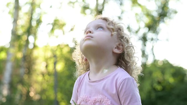 Portrait of a little beautiful curly-haired girl who looks into the sky. Slow motion