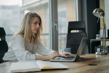Tired woman at her desk in the office. Young woman with tired face, disheveled hair works at the computer