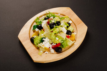 Greek salad with black olives and soft cheese on a wooden plate and dark background