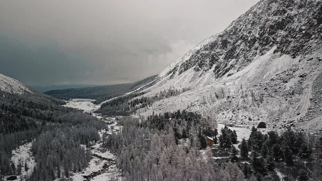The foot of the glacier of the huge Belukha mountain, the valley of the Aktru River, the Altai mountains. Cloudy weather, storm, wildlife, winter forest, frozen mountain river in the valley of the