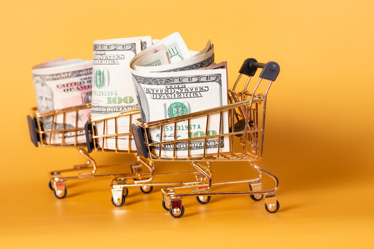 Shopping carts with dollars paper bills on a yellow background. Financial concept.
