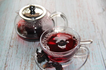 Hibiscus Red Hot tea in a glass mug and a clear glass teapot on a wooden table. View from above.