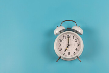  flat lay of white  vintage alarm clock shows 7 o clock  on blue  background.