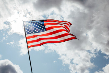 USA America flag waving in the wind over cloudy sky low angle view close up.