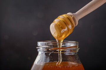 Honey dripping from honey dipper in glass jar.. Close-up. Healthy organic Thick honey dipping from...