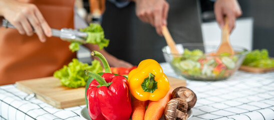Asian romantic couple using tongs lettuce and tomato on wooden chopping board into bowl while young man