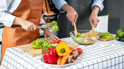 Asian romantic couple using tongs lettuce and tomato on wooden chopping board into bowl while young man