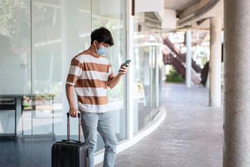 Fototapeta na wymiar Tourist man with luggage using smartphone to searching destination while wearing medical face mask to protection
