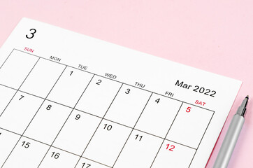 March 2022 calendar sheet with pen on pink background.