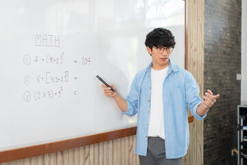 Male tutor standing in front of whiteboard and writing math equations on board to explaining new lesson