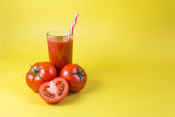 Tomato juice in a glass glass and red tomatoes on a yellow background place for text