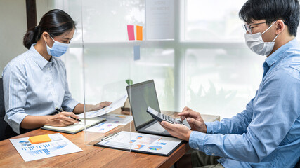Obraz premium Close up of two business colleagues holding document to record on notebook and using calculator to calculate