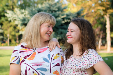 Female portrait of a beautiful plus size blond, blue-eyed mother and daughter in the park during summer. Family day, happy people concept