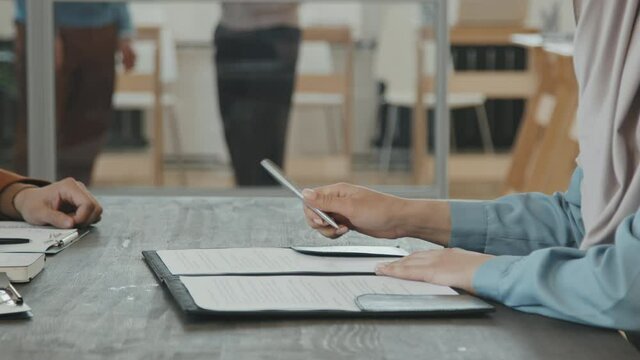 Tracking mid-section of unrecognizable Muslim woman in hijab singing document during board job interview