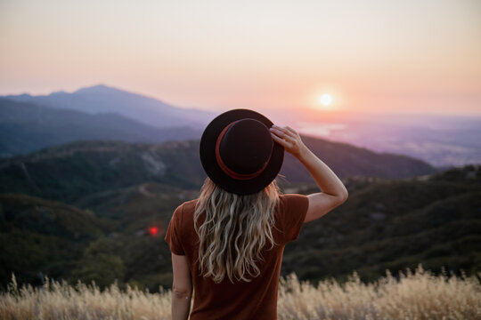 hipster girl wearing hat overlooking sunset in the mountains