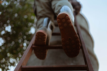 Gardening concept a male farmer wearing big boots climbing on a wooden ladder to a cement water tank