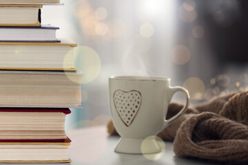 Stack of books and cup on table indoors. Bokeh effect
