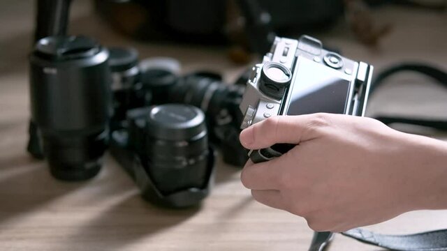Hand holding a vintage mirrorless camera and cleaning with brush, dusting and blowing air. keep the camera clean to take care prolong service life and surrounded by many lenses on wooden floor 4k 