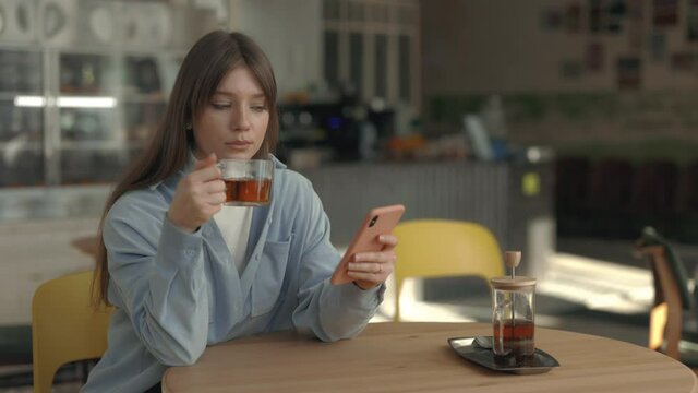 Caucasian woman drinking tea and using smartphone