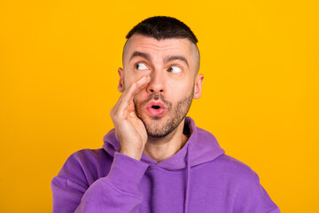 Photo of impressed millennial brunet guy look empty space wear purple hoodie isolated on yellow color background