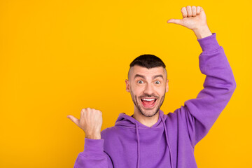 Photo portrait young man wearing purple hoody showing copyspace with thumb isolated vivid yellow color background