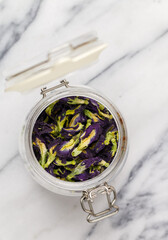 Glass jar with dry organic blue Anchan on marble background closeup. Herbal healthy tea. Butterfly pea tea, dry flowers. Thai cuisine. Selective focus, top view, copy space