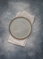 Obraz na płótnie Canvas empty grey plate and linen napkin on grey concrete or stone table. Cooking background. Rustic style. Selective focus. Top view, copy space