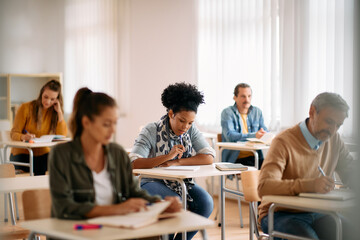 Mid adult black student and her classmates write an exam while attending class at lecture hall.