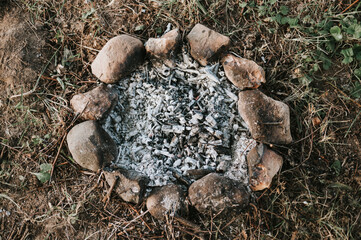 smoldering and ember gray coals and ashes from an extinct campfire in small children's bonfire made of stones on the ground on a summer or autumn evening. countryside and rustic scene. top view
