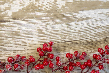 Christmas fir branch with berries and cones, sprinkled with snow on light wooden background close-up with copy space