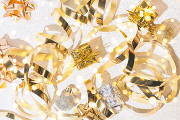 Decorative present boxes, balls, golden streamer and decorative bows on white glittering background.