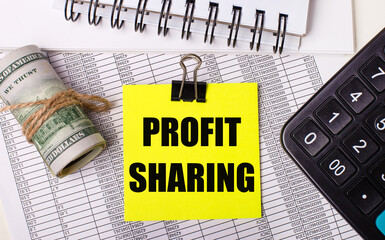 On the desktop there are reports, notepads, a calculator, a cash and a yellow sticker with the text PROFIT SHARING. Business concept