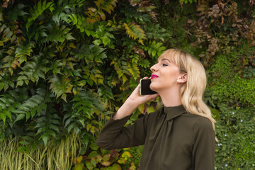 Entrepreneurial blonde girl in a business park in a corner of nature, smiling making a call, modern workplace