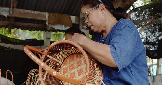 2 Cut in shot of Thai female farmers weave baskets in traditional Thai art patterns to sell as extra income in countryside of Thailand	
