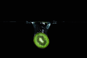 Kiwi falls into the water on a black background. Ripe and tasty kiwi. Kiwi cutaway