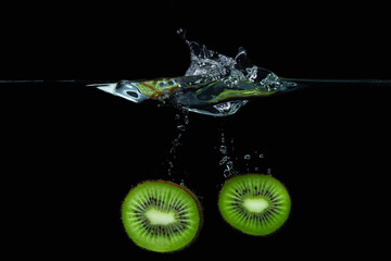 Kiwi falls into the water on a black background. Ripe and tasty kiwi. Kiwi cutaway