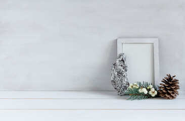 Christmas decoration, white frame mockup with spruce branches and a pine cone on a white table, copy space