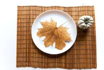 small pumpkin and dry brown maple leaf on white plate, autumn dinner table decor