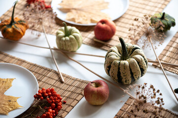 flat lay of small pumpkins and dry brown maple leafs on white plates, autumn dinner table decors........