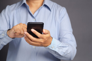 Businessman in a blue shirt holding a pen and using a smartphone while standing on a gray background. Close-up photo. Business, technology, and communication concept
