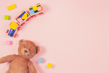 Baby kids toys frame with teddy bear, toy train, colorful wooden bricks on pastel pink background. Top view, flat lay