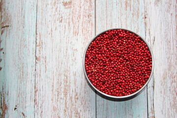 Brazilian red pepper pink or rose or red-aroeira, aroeira-pementeira or rosa-poivre (schinus terebinthifolius) in a metallic bowl on a wooden table. View from above.